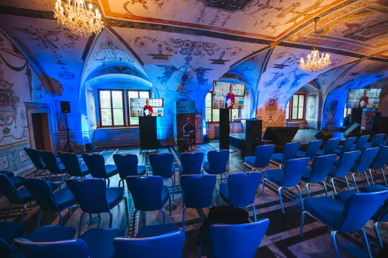 Conference seating and presentation screens beneath blue-lit painted palace vaults
