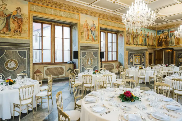Round banquet tables with floral centrepieces beneath chandeliers in a painted hall