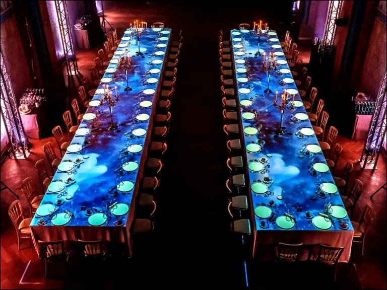 Long blue-lit tables arranged for a dramatic gala dinner
