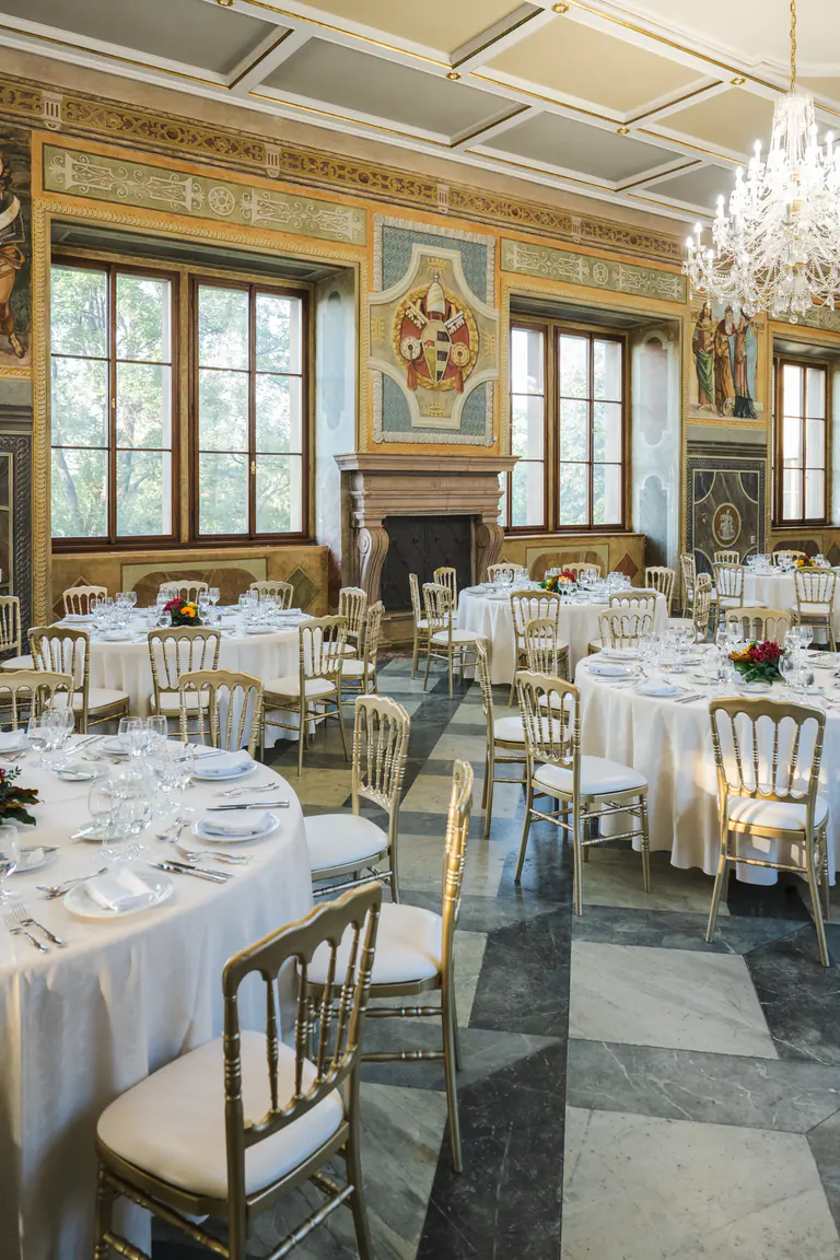 White table settings, flowers and a chandelier beneath a painted palace ceiling